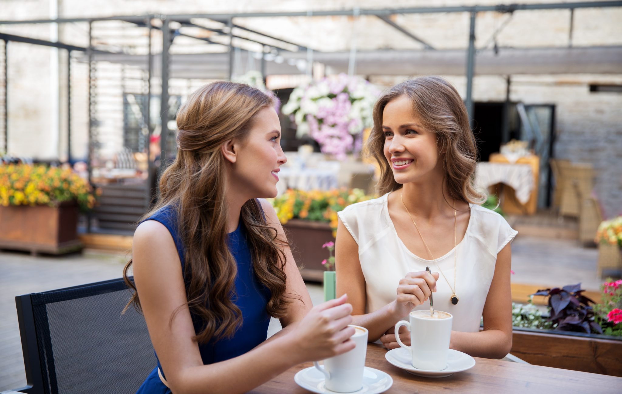 communication and friendship concept - smiling young women drinking coffee at street cafe